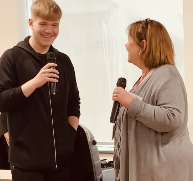 A young man and a woman laugh, both holding microphones during an interview